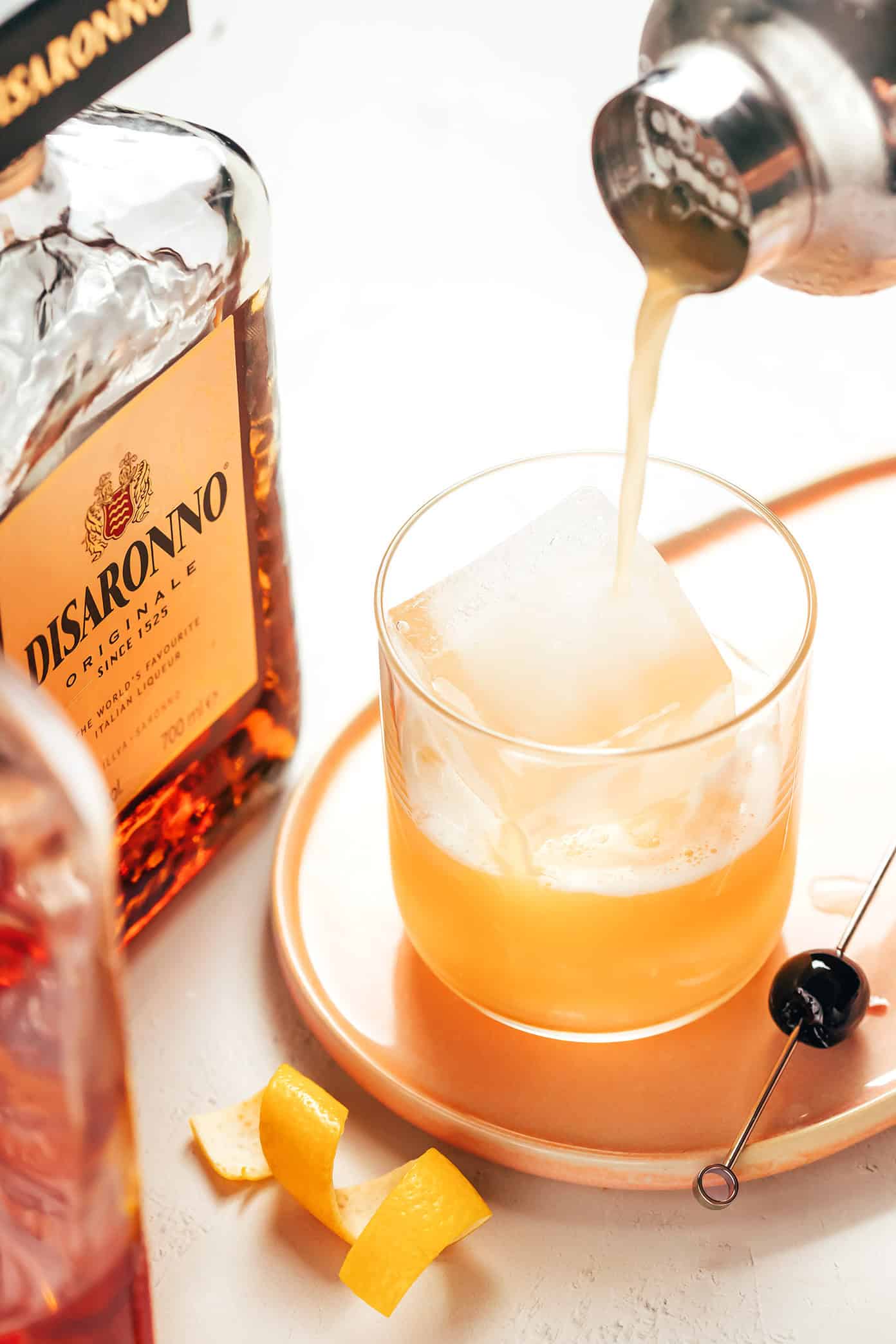 This classic Amaretto Sour recipe is easy to make with bourbon, lemon juice, Amaretto and egg white. Feel free to add additional sweetener or bitters, if you'd like, and garnish with a lemon twist and maraschino cherry. It's always such a cozy and sophisticated cocktail! | gimmesomeoven.com How to make an amaretto sour cocktail