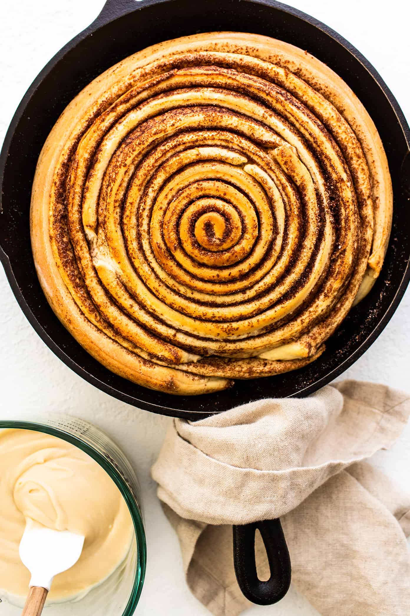 This giant cinnamon roll recipe is made with the most delicious soft dough, cinnamon-sugar filling, and a tangy cream cheese icing. Ready to go for breakfast or brunch in one hour from start to finish! | gimmesomeoven.com Unfrosted giant cinnamon roll in skillet with cream cheese frosting