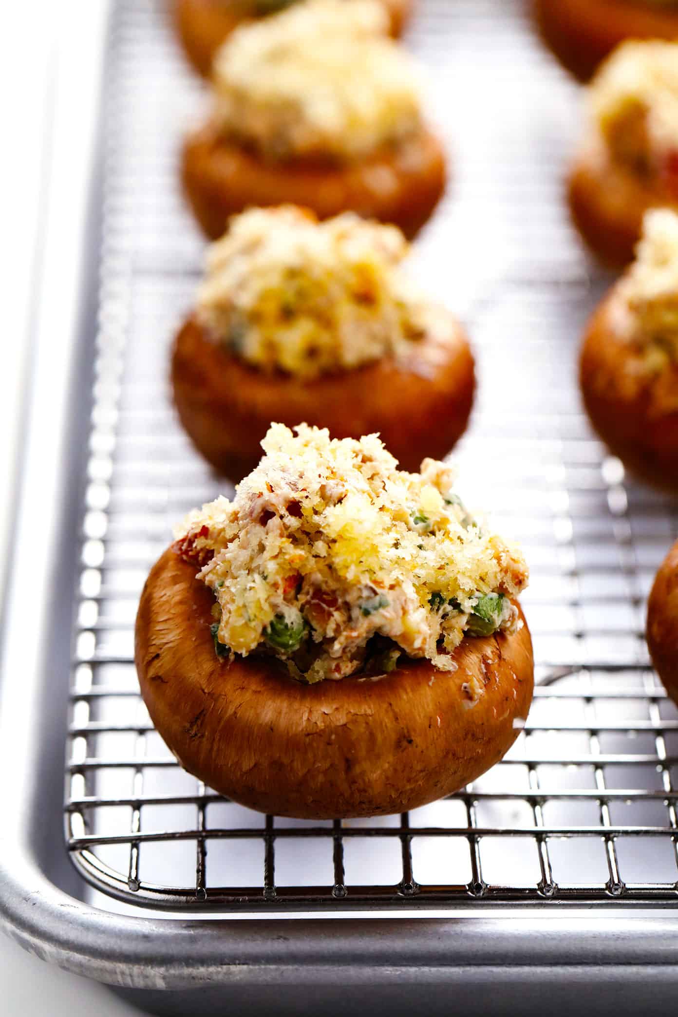 This easy stuffed mushrooms recipe is made with a garlicky goat cheese, sun-dried tomato, pine nut and basil filling and topped with crispy toasted breadcrumbs. The perfect vegetarian appetizer that's easy to make ahead of time (up to 1 day in advance) and always a crowd fave! | gimmesomeoven.com Stuffed Mushrooms on Wire Rack Before Baking