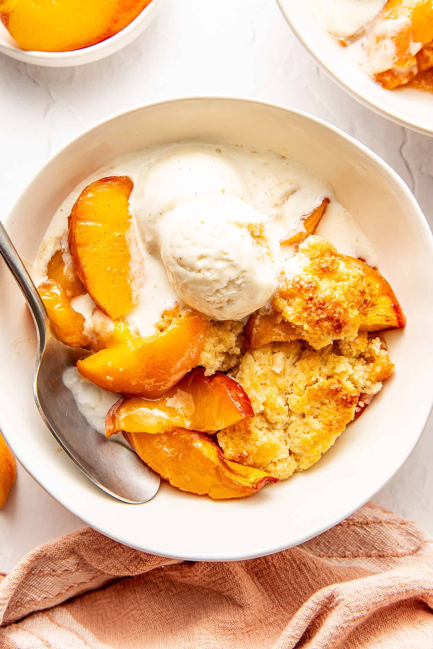 This easy peach cobbler recipe features a juicy cinnamon-vanilla peach filling and a golden buttery biscuit topping -- the perfect dessert to celebrate fresh peach season! | gimmesomeoven.com fresh peach cobbler in a bowl with melty vanilla ice cream