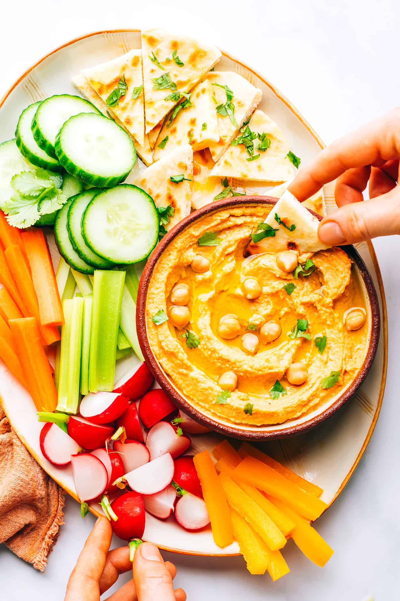 This Thai-inspired red curry hummus recipe is quick and easy to make in just 10 minutes with chickpeas, tahini, coconut milk, curry paste, ginger and garlic. Serve it up as a dip with cruditรฉs and naan, or use it as a spread on burgers or wraps. Such a great easy appetizer! | gimmesomeoven.com Thai Red Curry Hummus on Platter with Crudites and Naan